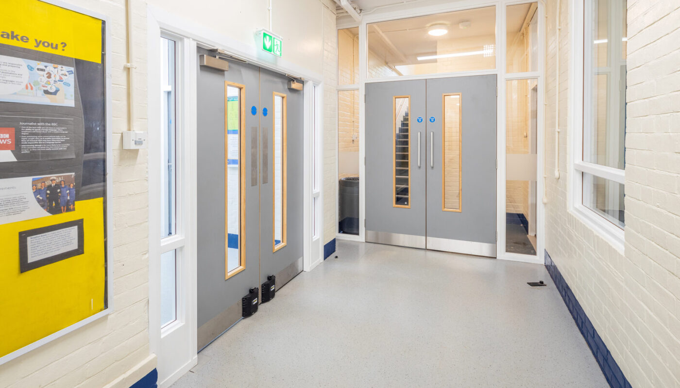 Grey fire doors for schools with vision panels and kick plates in a school corridor